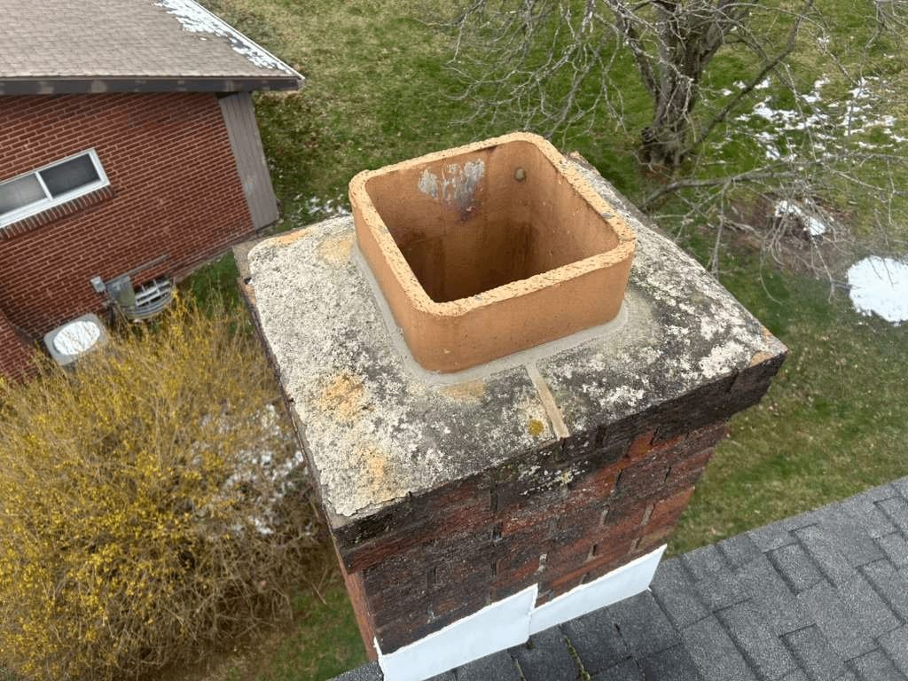 Cracked, lichen-covered chimney crown with no cap on a Pittsburgh brick chimney before repair