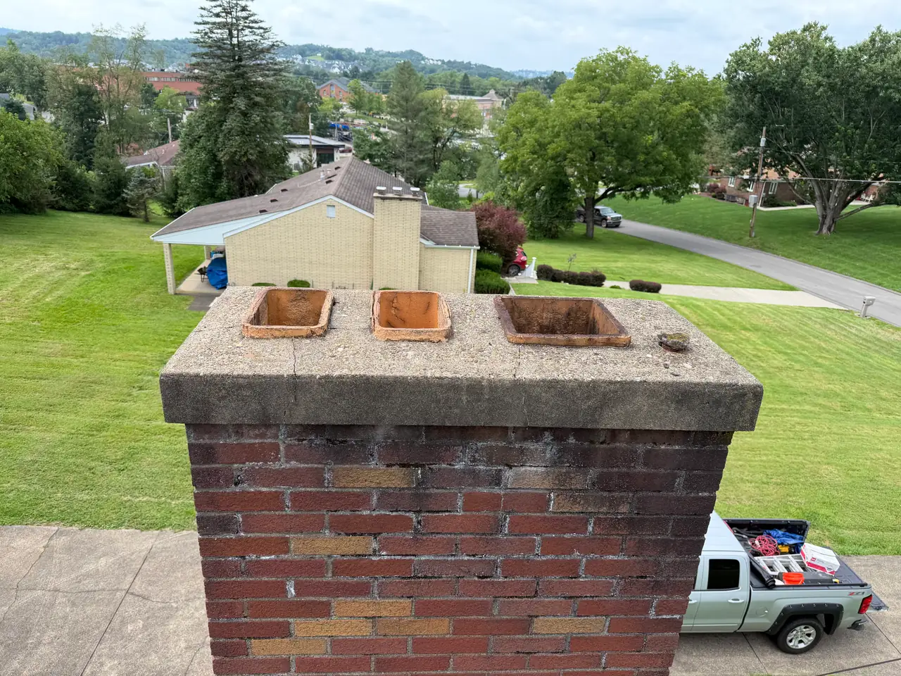 Before repair: a weathered Canonsburg, PA chimney crown with cracks and lichen, and three clay flue tiles standing completely uncapped