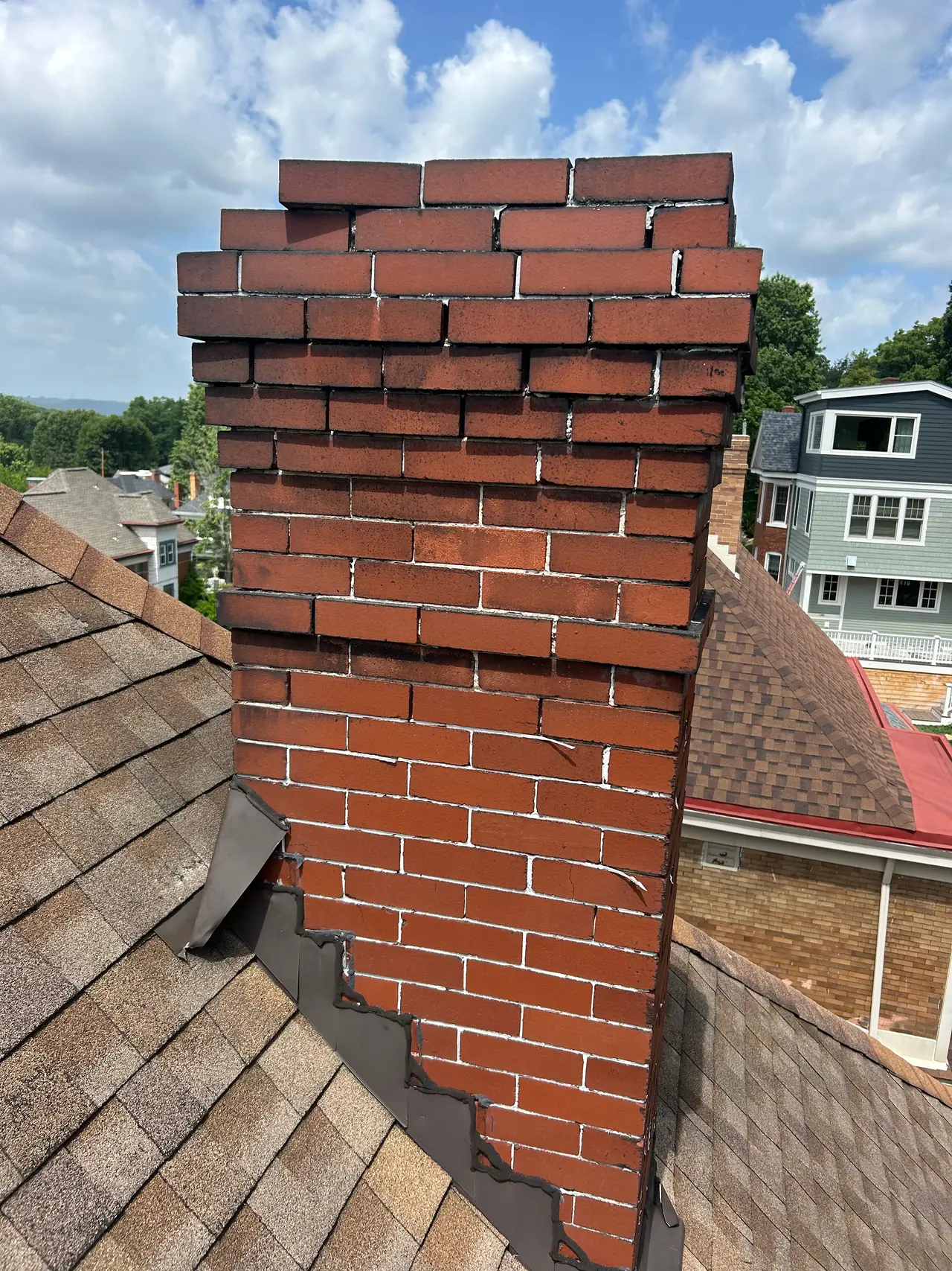 Close view of worn mortar joints and spalling on a red brick chimney where it meets the roof flashing in Pittsburgh